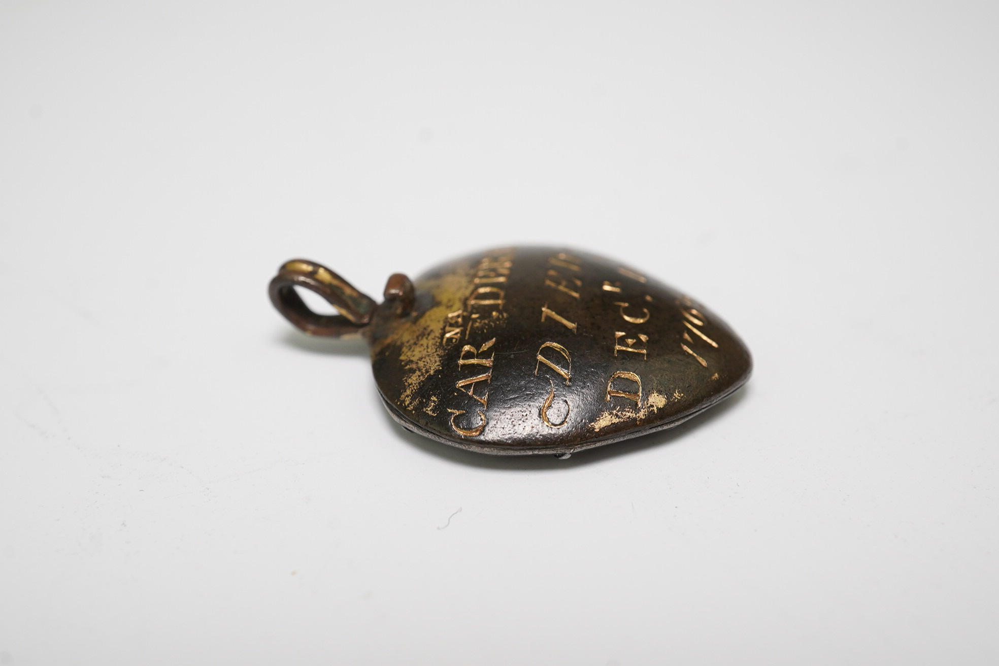 An 18th century gilt metal heart shaped mourning pendant, with engraved inscription, 'CARna DERBY DIED DEC 11th, 1762' and plaited hair beneath a glazed panel verso, 27mm.